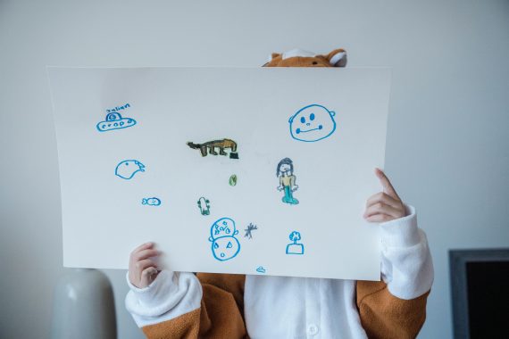 A child in a costume holds a playful drawing with colorful sketches, expressing creativity.