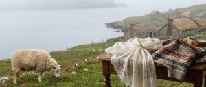 Panorama delle Isole Shetland con pecora al pascolo, scialle di pizzo sottile che passa in una fede nuziale e maglia Fair Isle su un tavolo di legno.