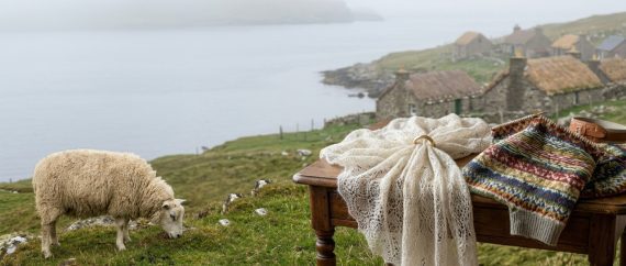 Panorama delle Isole Shetland con pecora al pascolo, scialle di pizzo sottile che passa in una fede nuziale e maglia Fair Isle su un tavolo di legno.